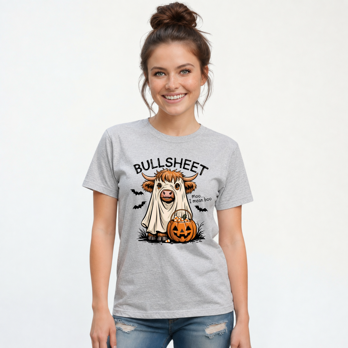 Woman modeling a Sports Gray T-shirt with the Bullsheet Halloween Highland cow ghost and jack-o'-lantern design.