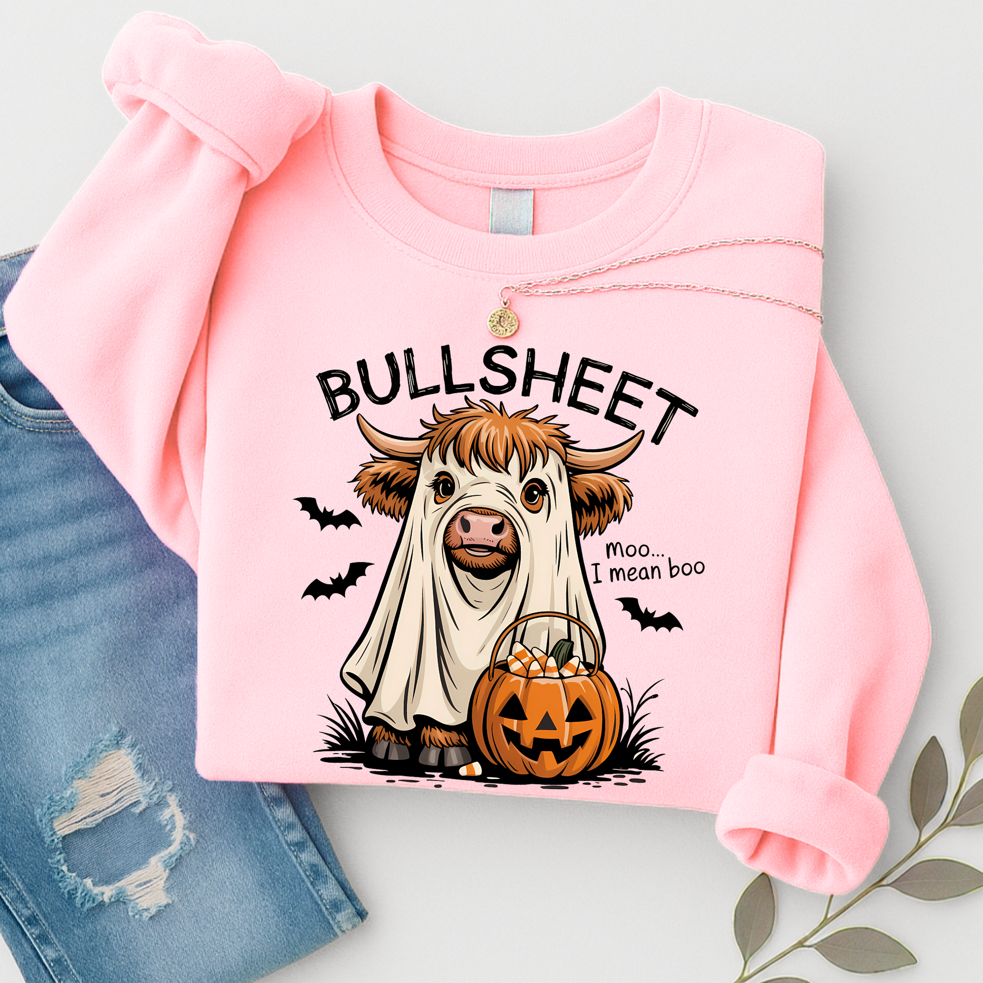 Pink sweatshirt with a ghostly cow holding a pumpkin and 'BULLSHEET moo I mean boo' text, displayed with jeans on a light gray background.
