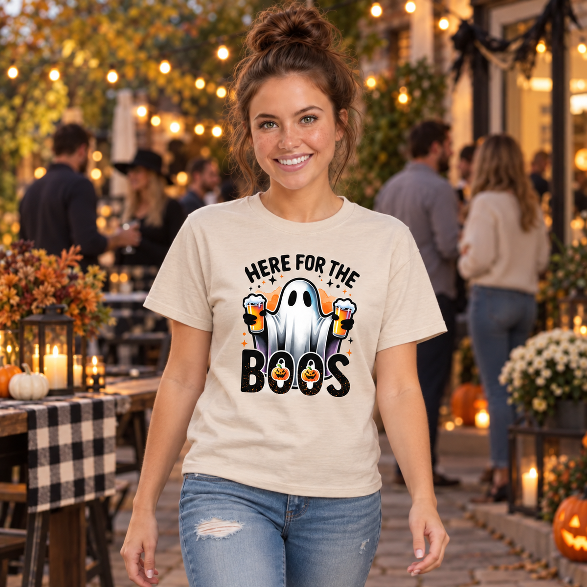 Woman wearing a sand T-shirt featuring a ghost with two beer mugs and Here For The Boos text at a Halloween party.