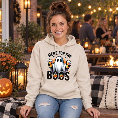 Woman seated in a sand hoodie with a ghost holding two beer mugs and Here For The Boos design at a Halloween party.