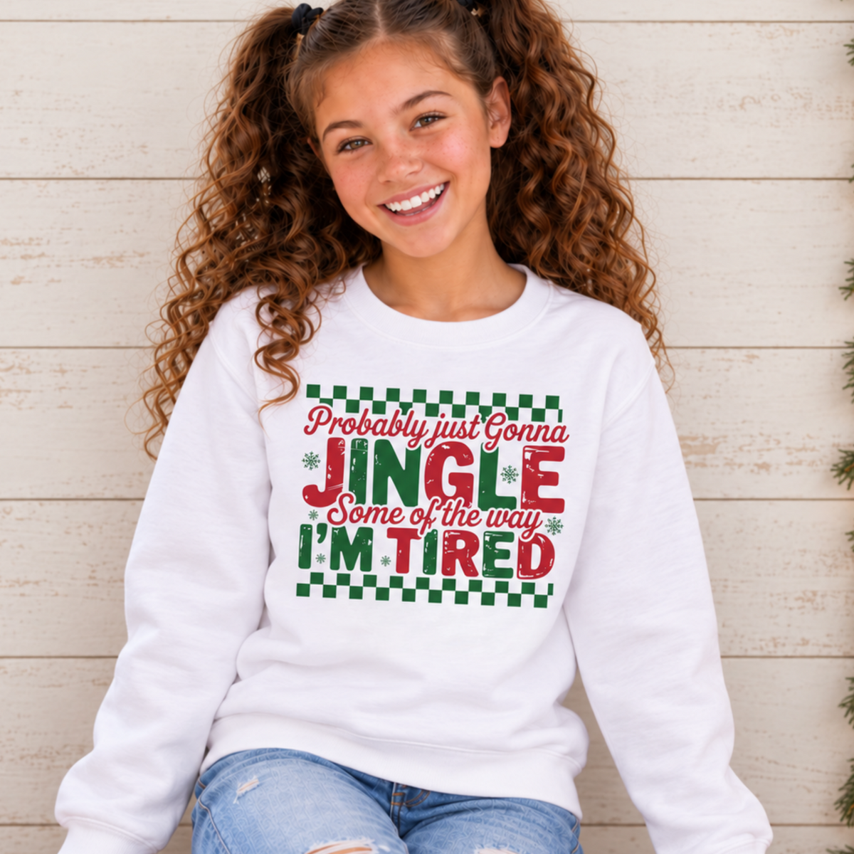 Girl wearing a white youth sweatshirt with red and green Probably Just Gonna Jingle Some of the Way I'm Tired Christmas design by a café window