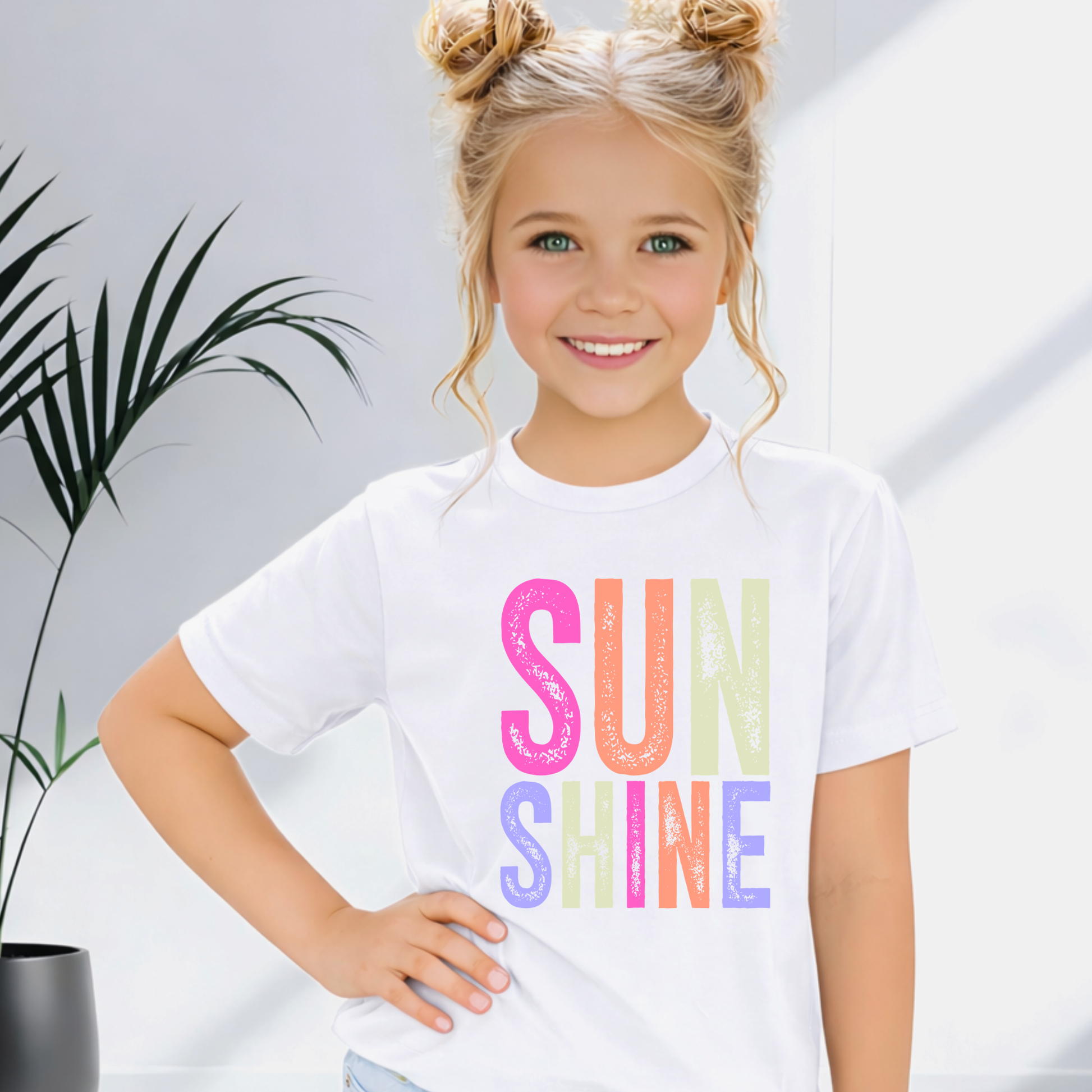 Child wearing a white t-shirt with 'SUN SHINE' in colorful letters, standing indoors.