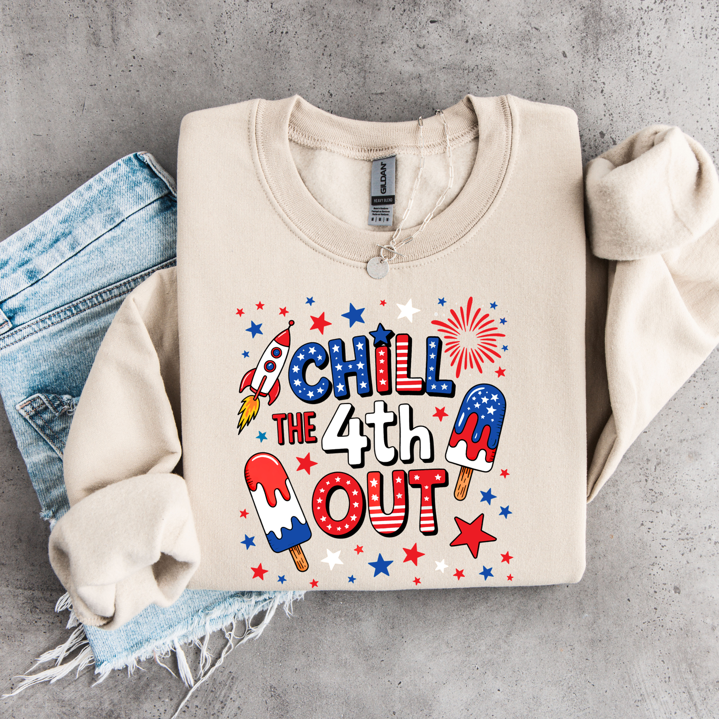 Beige sweatshirt with 'Chill the 4th Out' design on a concrete surface with jeans.