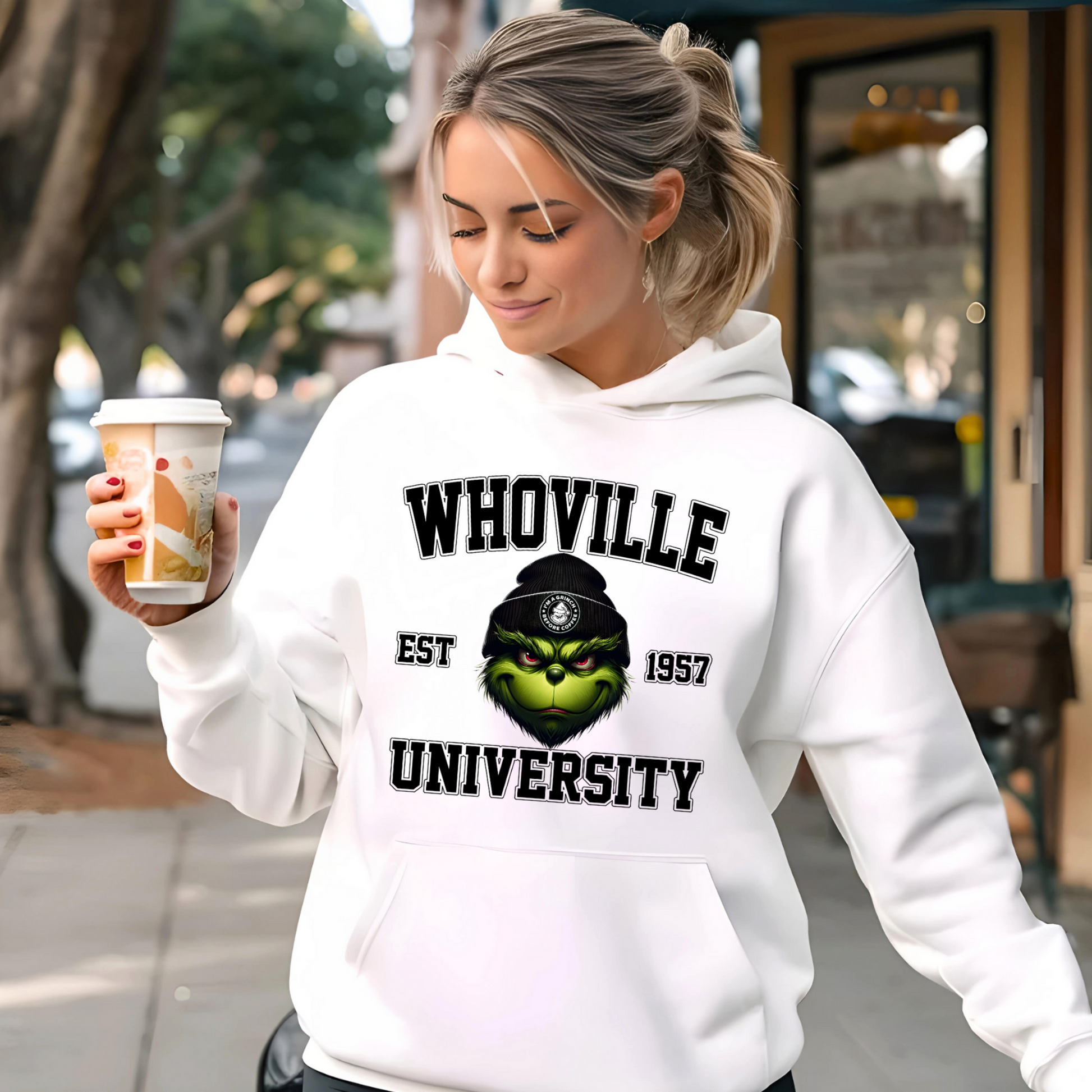 White hoodie with Whoville University graphic worn outdoors with coffee.