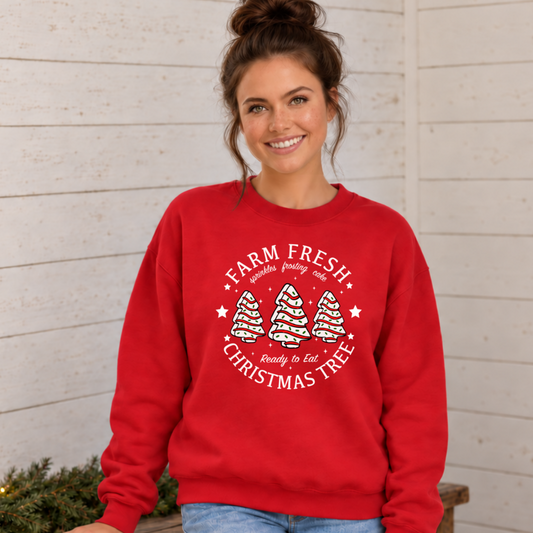 Woman wearing a red Farm Fresh Christmas Tree Cakes graphic sweatshirt against a light shiplap wall.