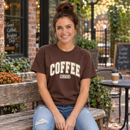 Woman modeling a brown T-shirt with "COFFEE WEATHER" printed in cream varsity lettering on the front against a white background.