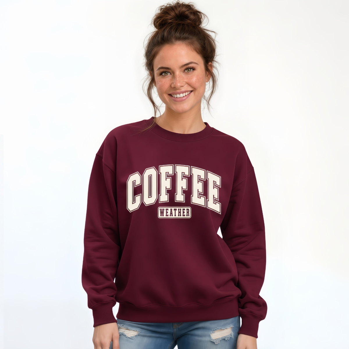 Woman wearing a maroon crewneck sweatshirt with "COFFEE WEATHER" printed in cream and brown block letters on the front.