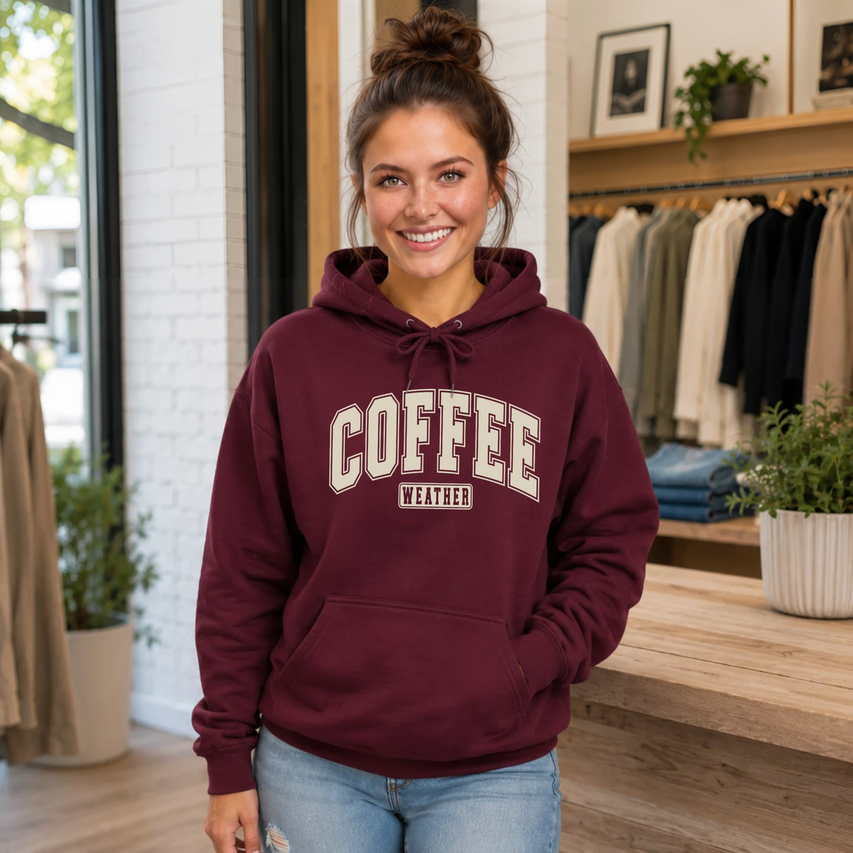 Woman indoors wearing a maroon “Coffee Weather” crewneck sweatshirt and jeans.