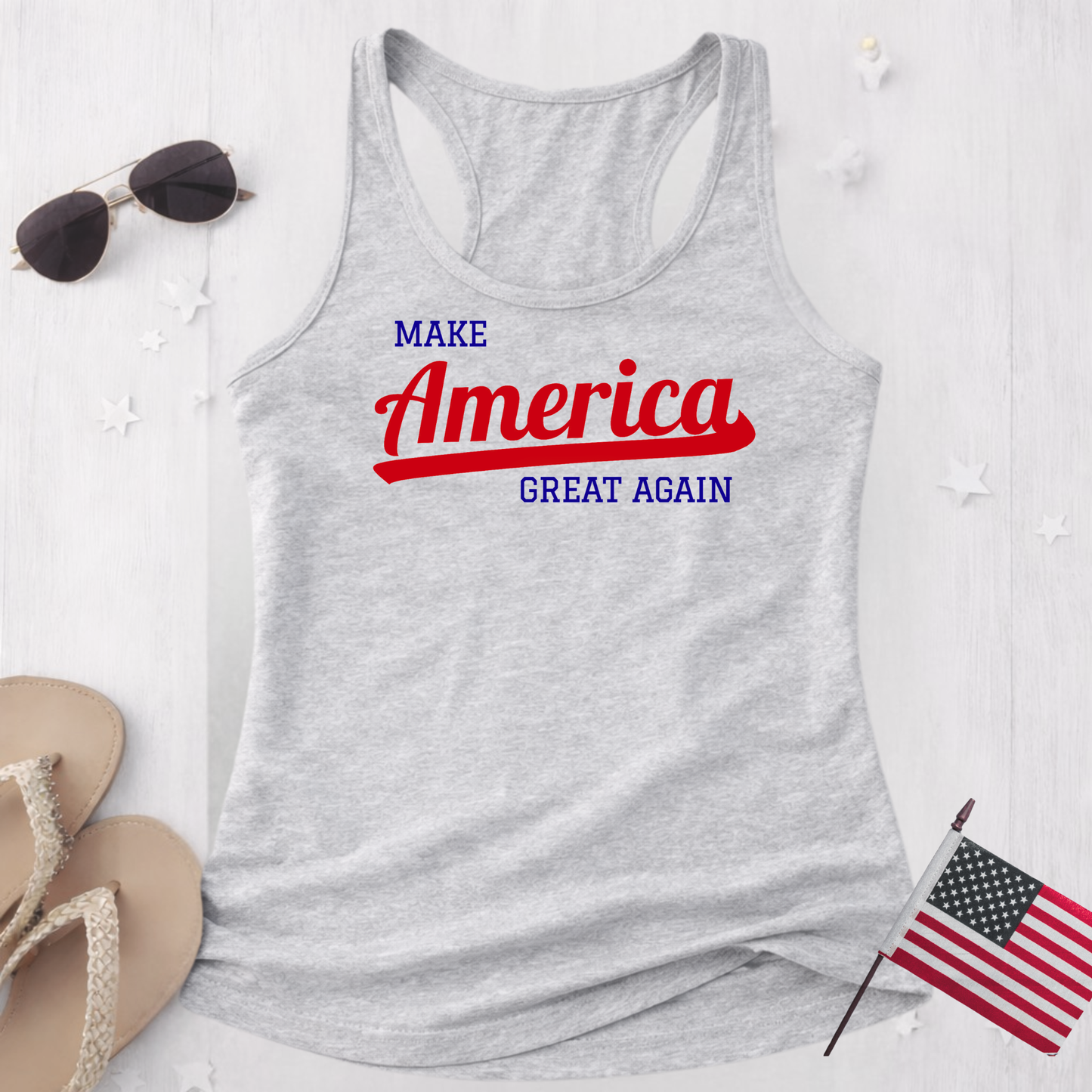 Sports gray women’s racerback tank top flat lay with Make America Great Again patriotic graphic, styled with sunglasses, sandals, and American flag