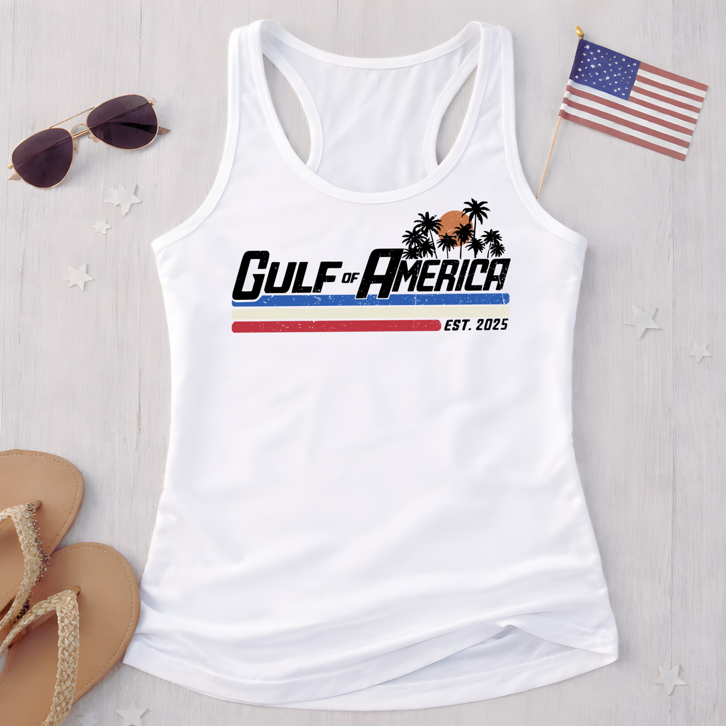White women’s racerback tank top flat lay with Gulf of America graphic, styled with sunglasses, sandals and American flag