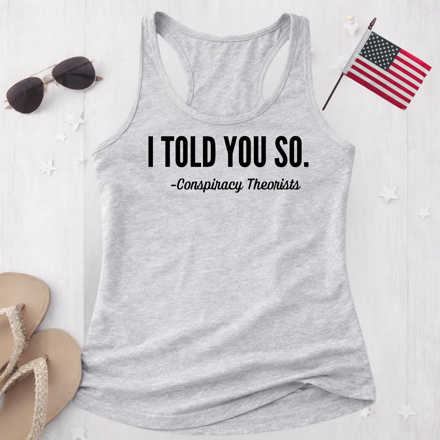 Gray tank top with 'I Told You So. - Conspiracy Theorists' text, sunglasses, and American flag on a white background