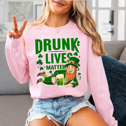 Woman posing in a light pink St. Patrick’s Day sweatshirt that reads “Drunk Lives Matter” with shamrock and leprechaun design