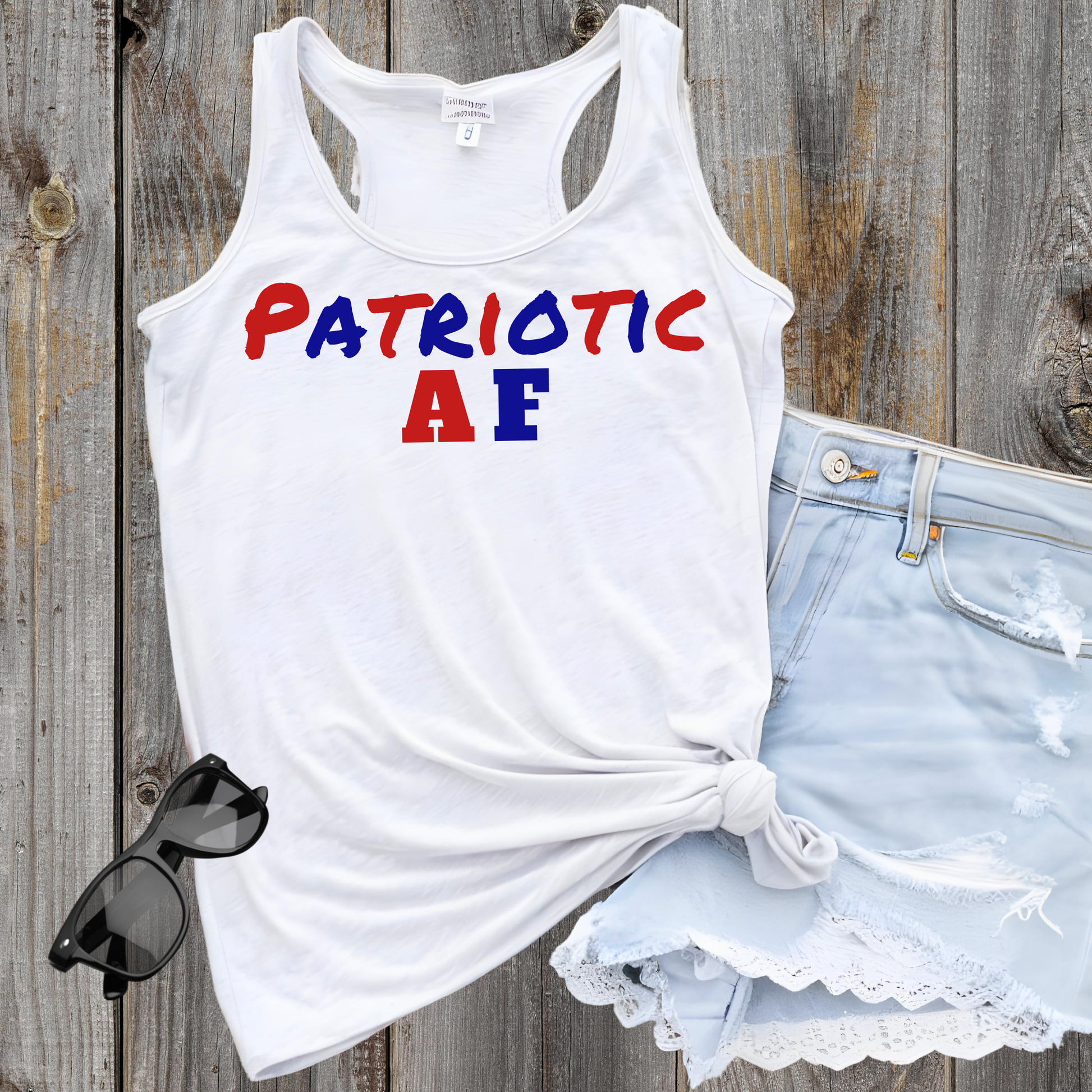 Flat lay of "Patriotic AF" tank with denim shorts and sunglasses