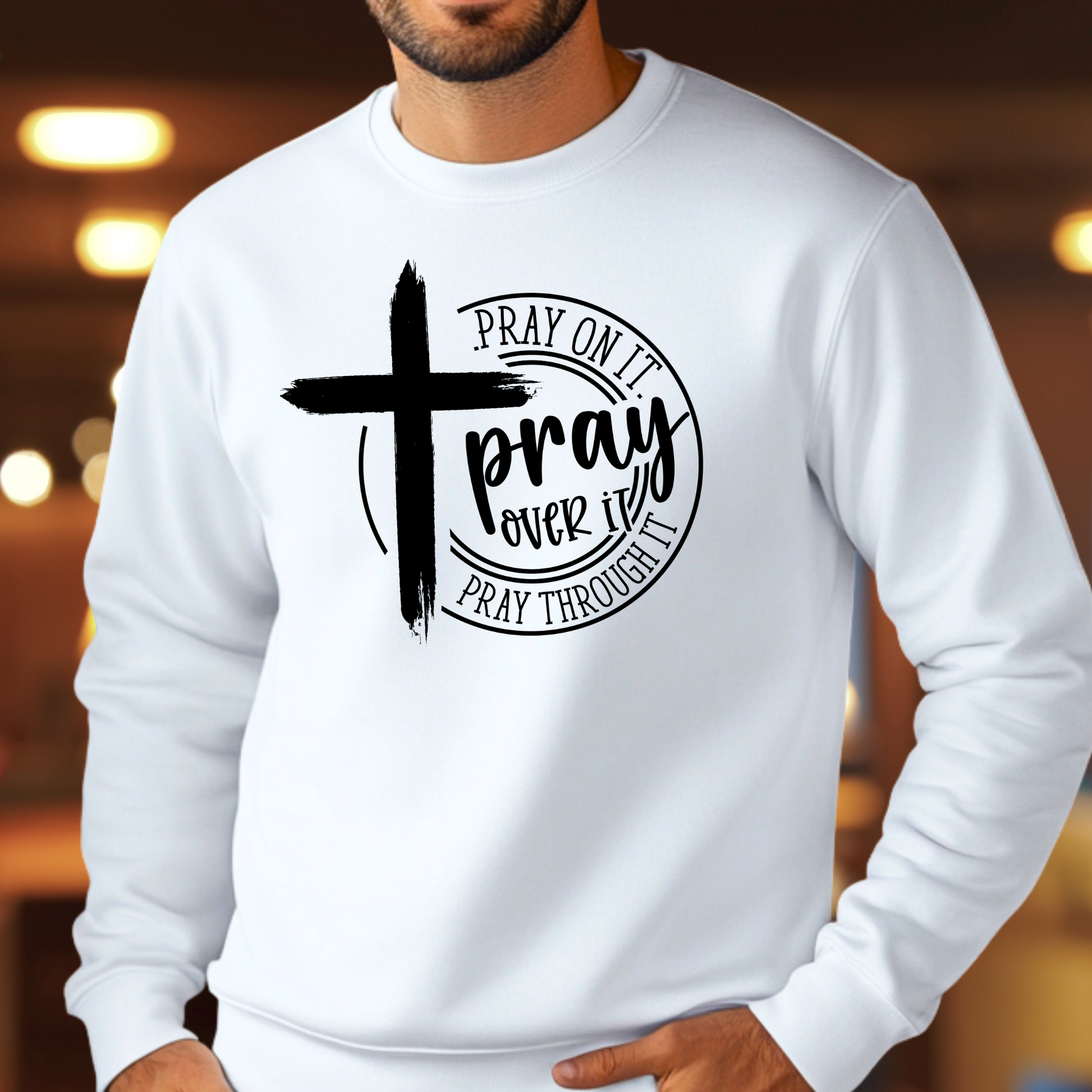 Man wearing a white sweatshirt with a bold white cross and text: "Pray On It, Pray Over It, Pray Through It"