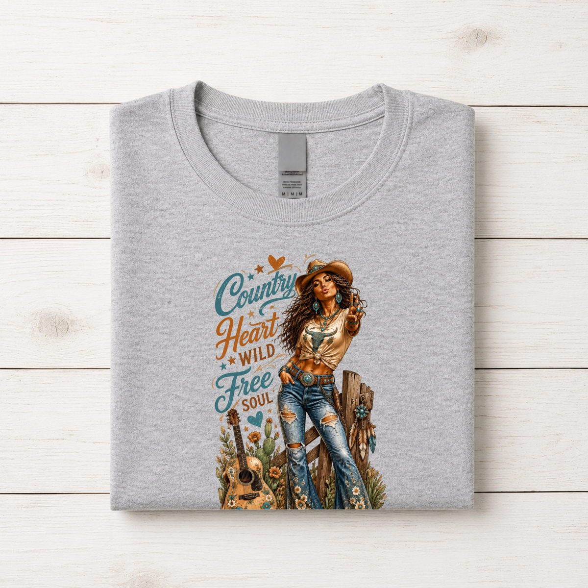 Folded sports gray youth T-Shirt displaying the Country Heart Wild Free Soul cowgirl design on a light wood flat lay background.