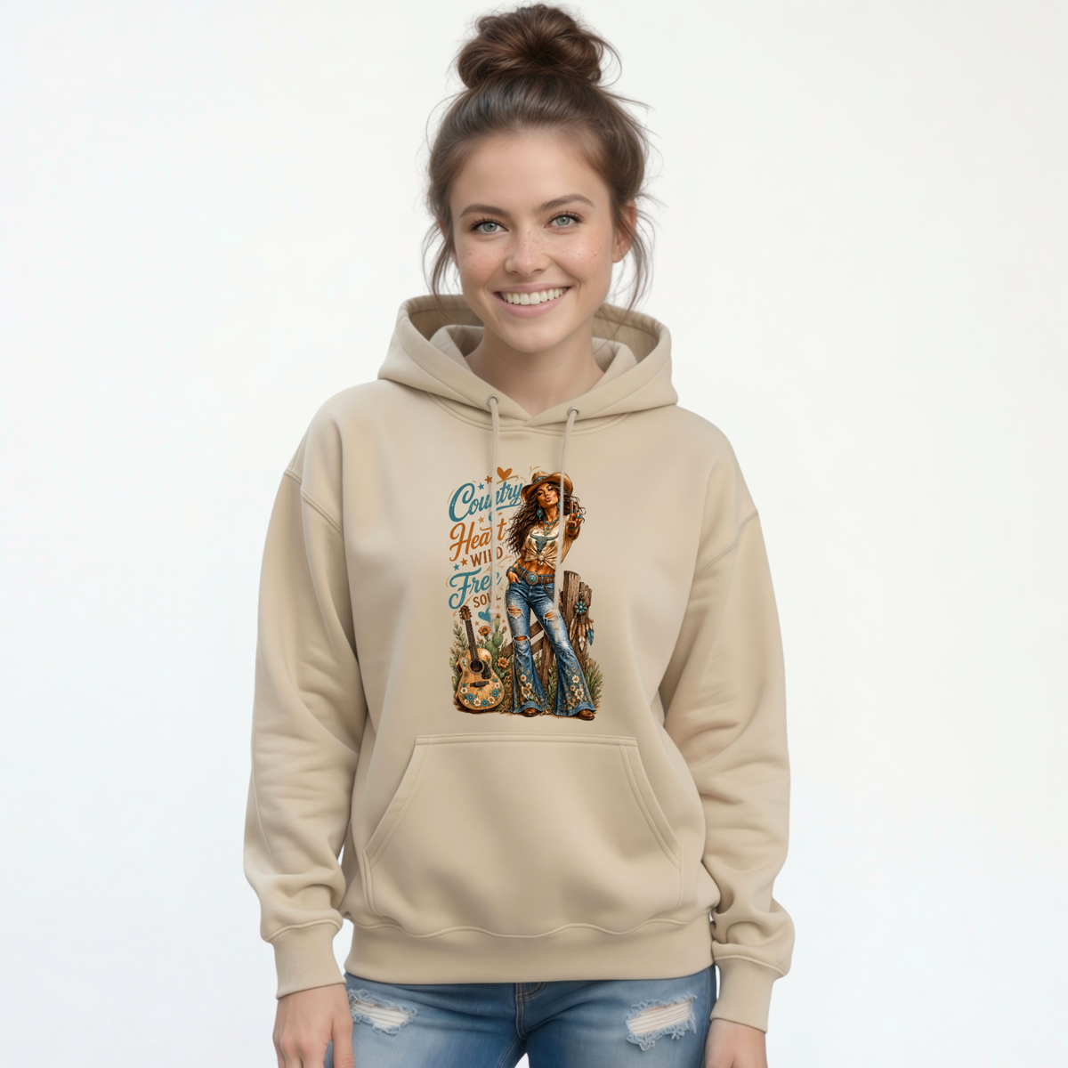 Smiling woman wearing a sand hoodie with the Country Heart Wild Free Soul cowgirl, guitar and floral design on a white background.