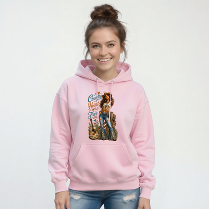 Woman wearing a light pink hoodie printed with the Country Heart Wild Free Soul country cowgirl design against a white studio backdrop.