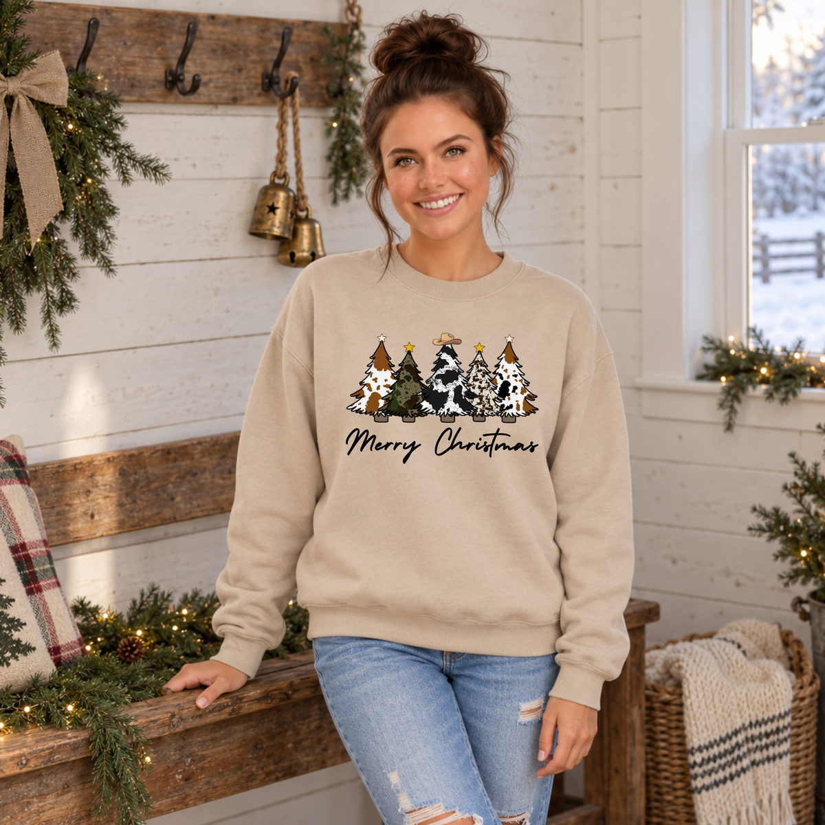 Woman wearing a sand Merry Christmas cow print trees sweatshirt beside a decorated farmhouse bench.