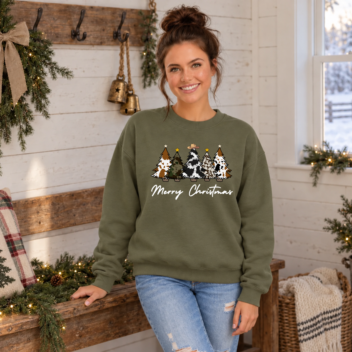 Woman modeling a military green cow print Christmas trees sweatshirt beside a holiday bench.
