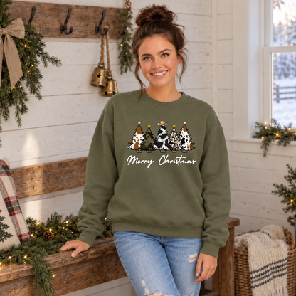 Woman modeling a military green cow print Christmas trees sweatshirt beside a holiday bench.