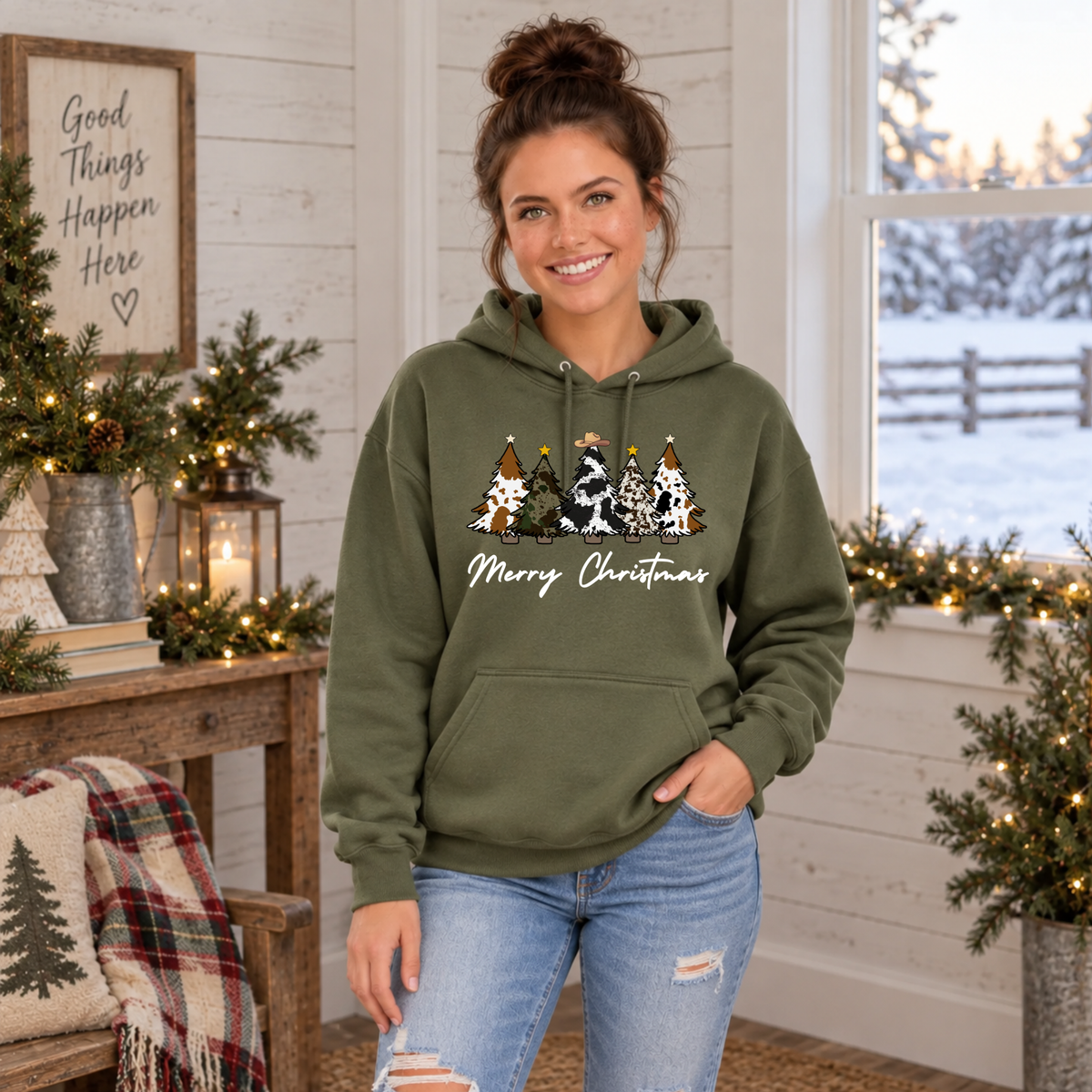 Woman wearing a military green Merry Christmas cow print trees hoodie in a farmhouse room.