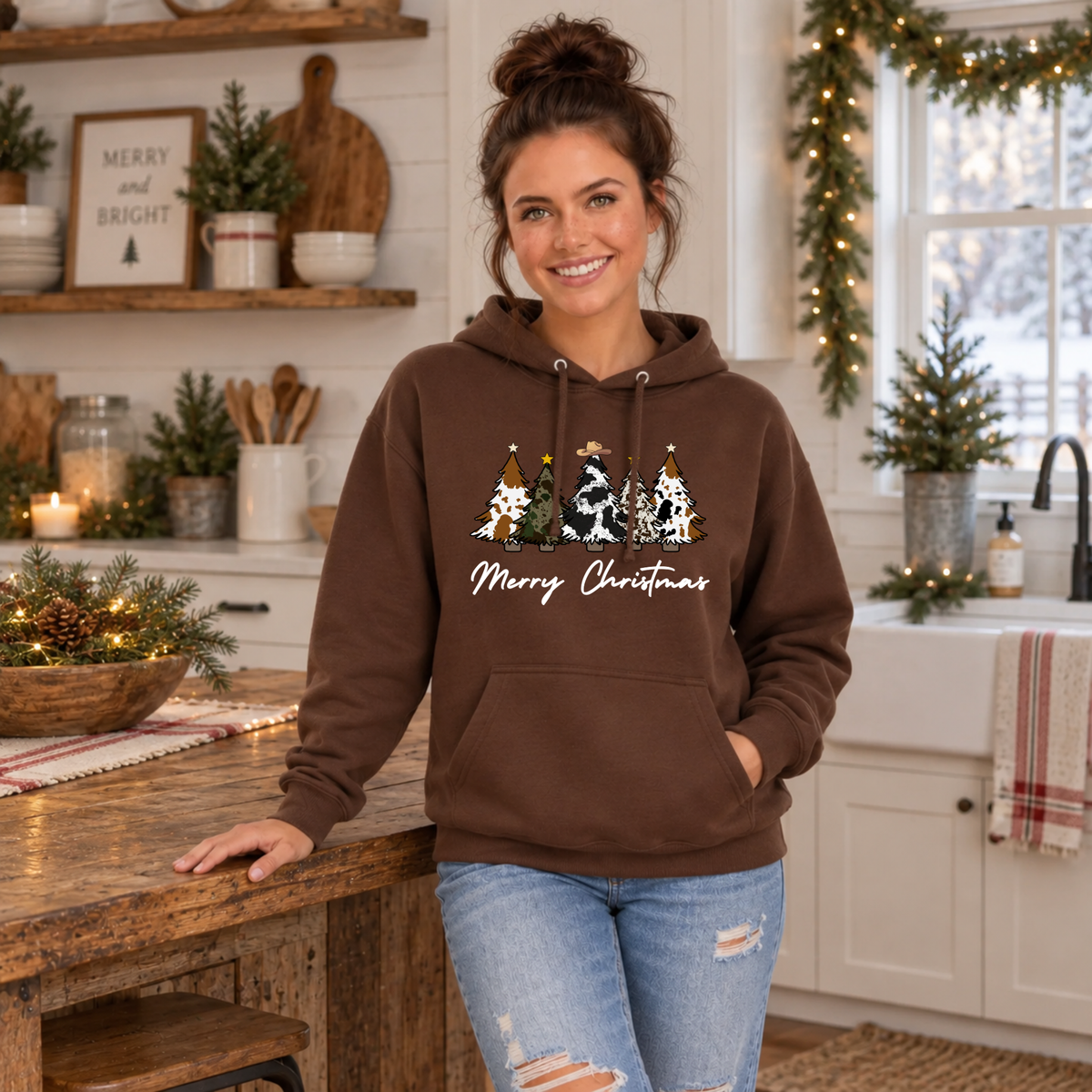Woman modeling a brown cow print Christmas trees hoodie in a festive kitchen.