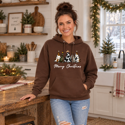 Woman modeling a brown cow print Christmas trees hoodie in a festive kitchen.