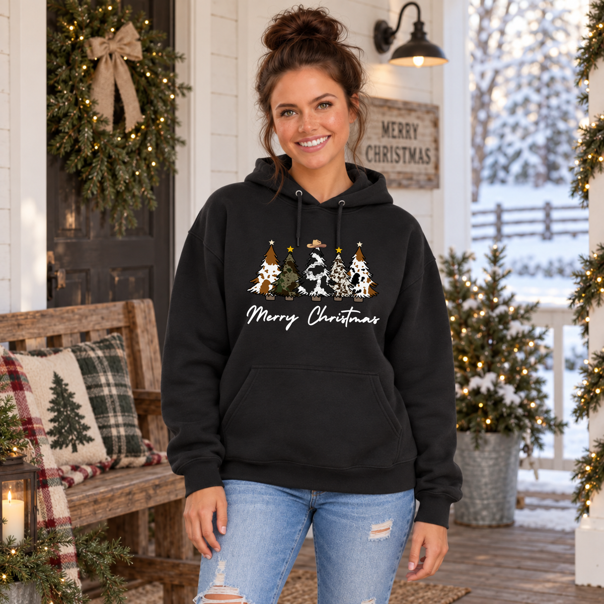 Woman wearing a black Merry Christmas cow print trees hoodie beside a decorated bench.