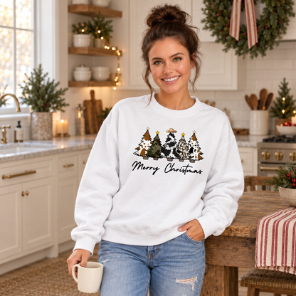 Woman modeling a white cow print Christmas trees sweatshirt in a holiday kitchen.