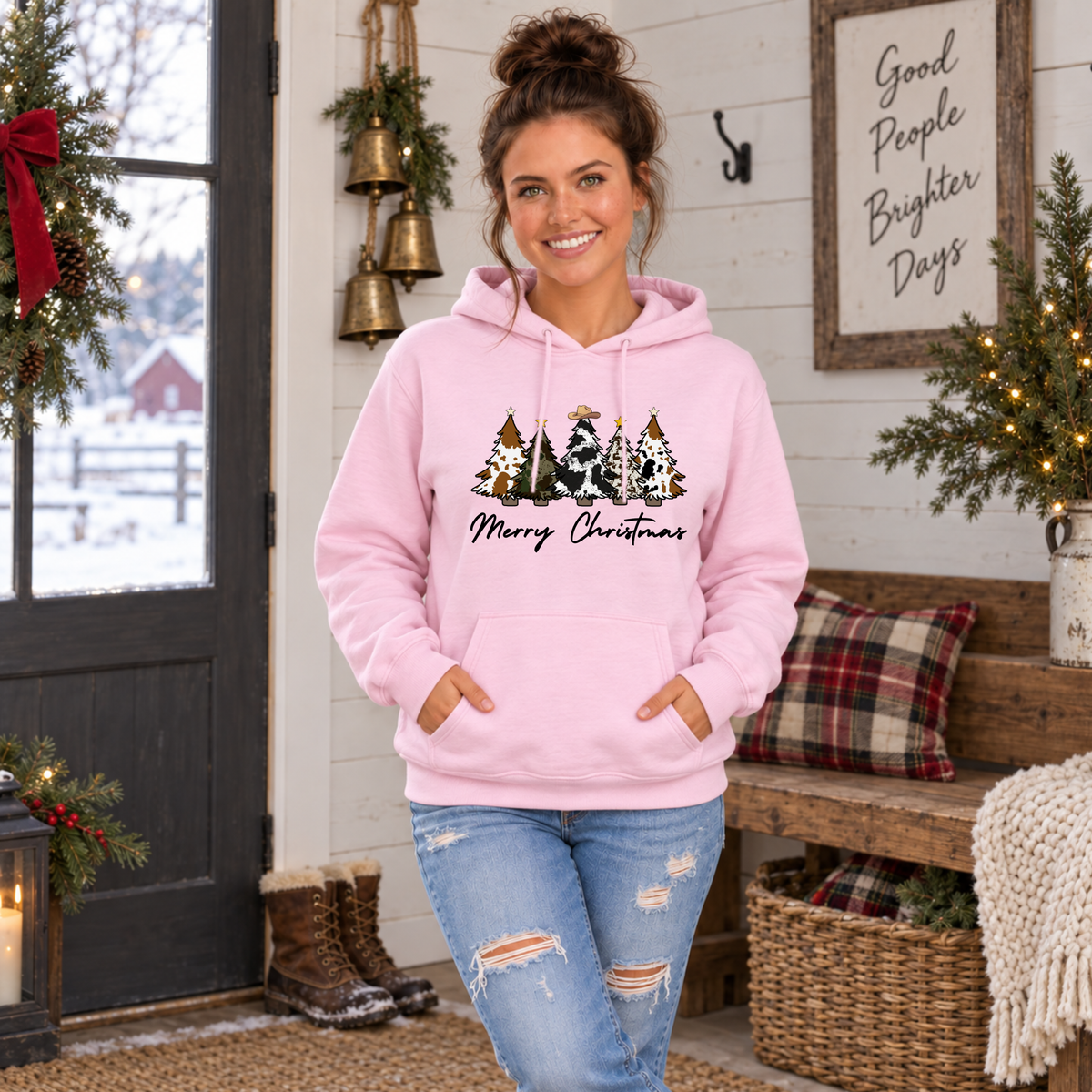 Woman modeling a light pink cow print Christmas trees hoodie in a farmhouse holiday room.