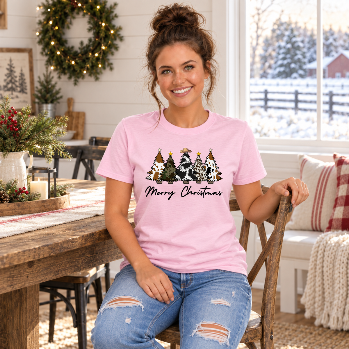Woman seated in a light pink cow print Christmas trees T-shirt in a holiday dining room.