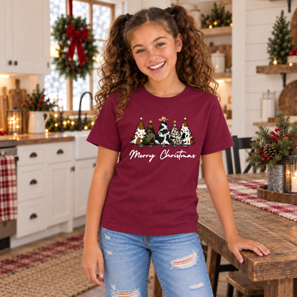 Girl wearing a maroon cow print Christmas trees T-shirt beside a decorated farmhouse table.