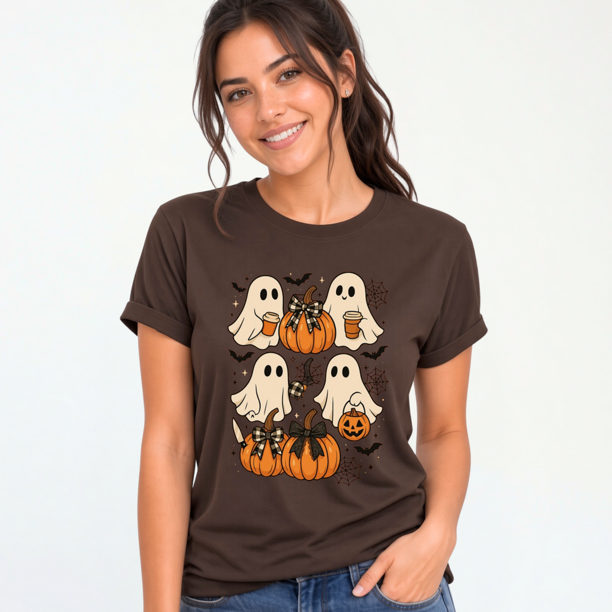 A woman wearing a dark brown short-sleeve t-shirt with a Halloween graphic of four white ghosts and orange pumpkins, paired with blue jeans, against a plain white background.