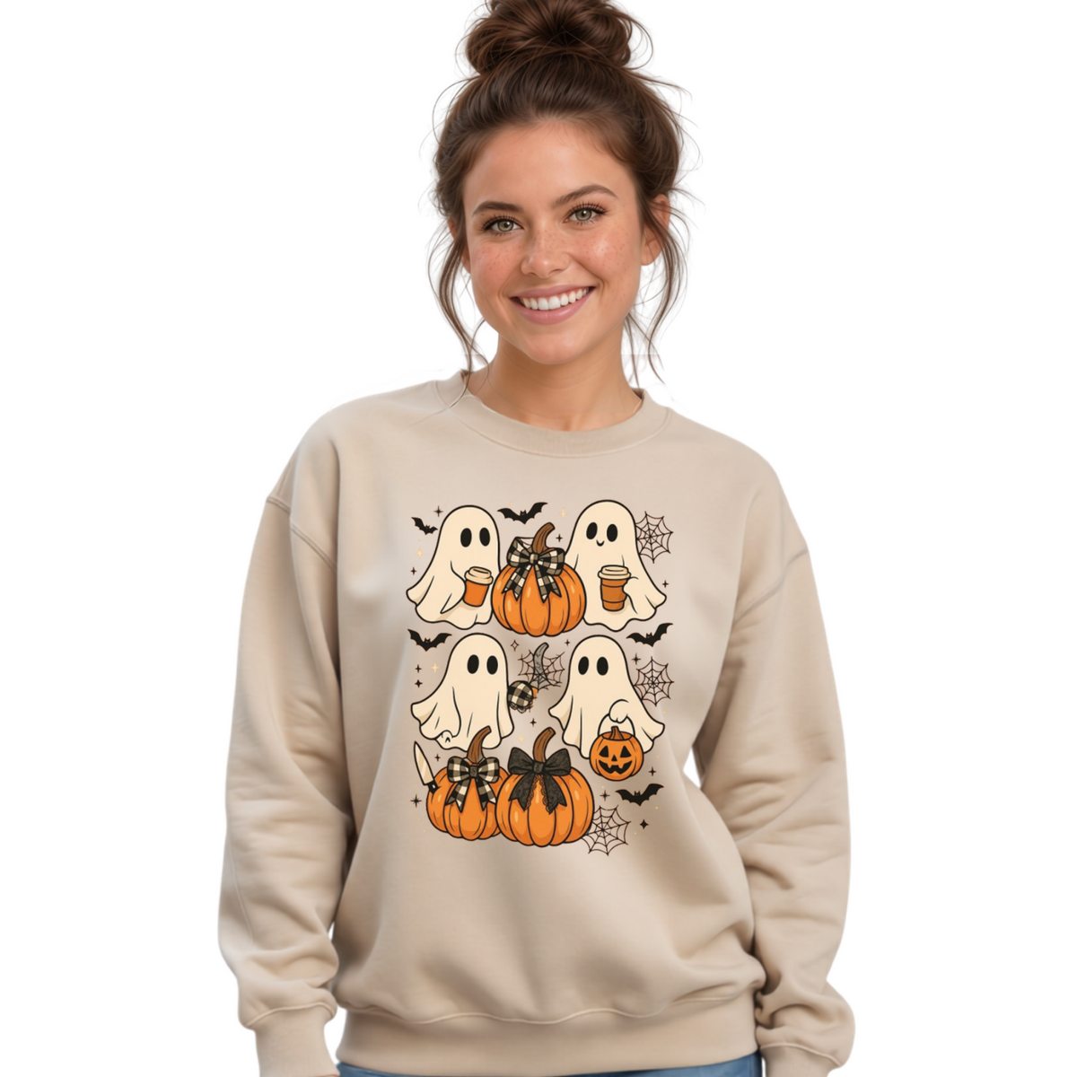 A woman wearing a beige crewneck sweatshirt with a Halloween graphic of cartoon ghosts, pumpkins, bats, and a spider, paired with distressed blue jeans, against a plain white background.