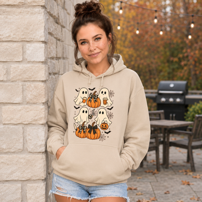 A woman wearing a beige pullover hoodie with a Halloween graphic print featuring cartoon ghosts, pumpkins, bats, and spiderwebs, paired with blue jeans against a plain white background.