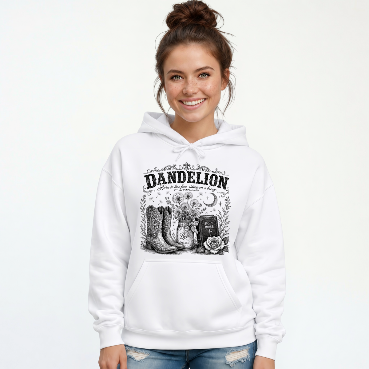 Woman wearing a white Dandelion pullover hoodie with cowboy boots, dandelion-filled mason jar, Holy Bible, rose, and crescent moon graphic on a white background