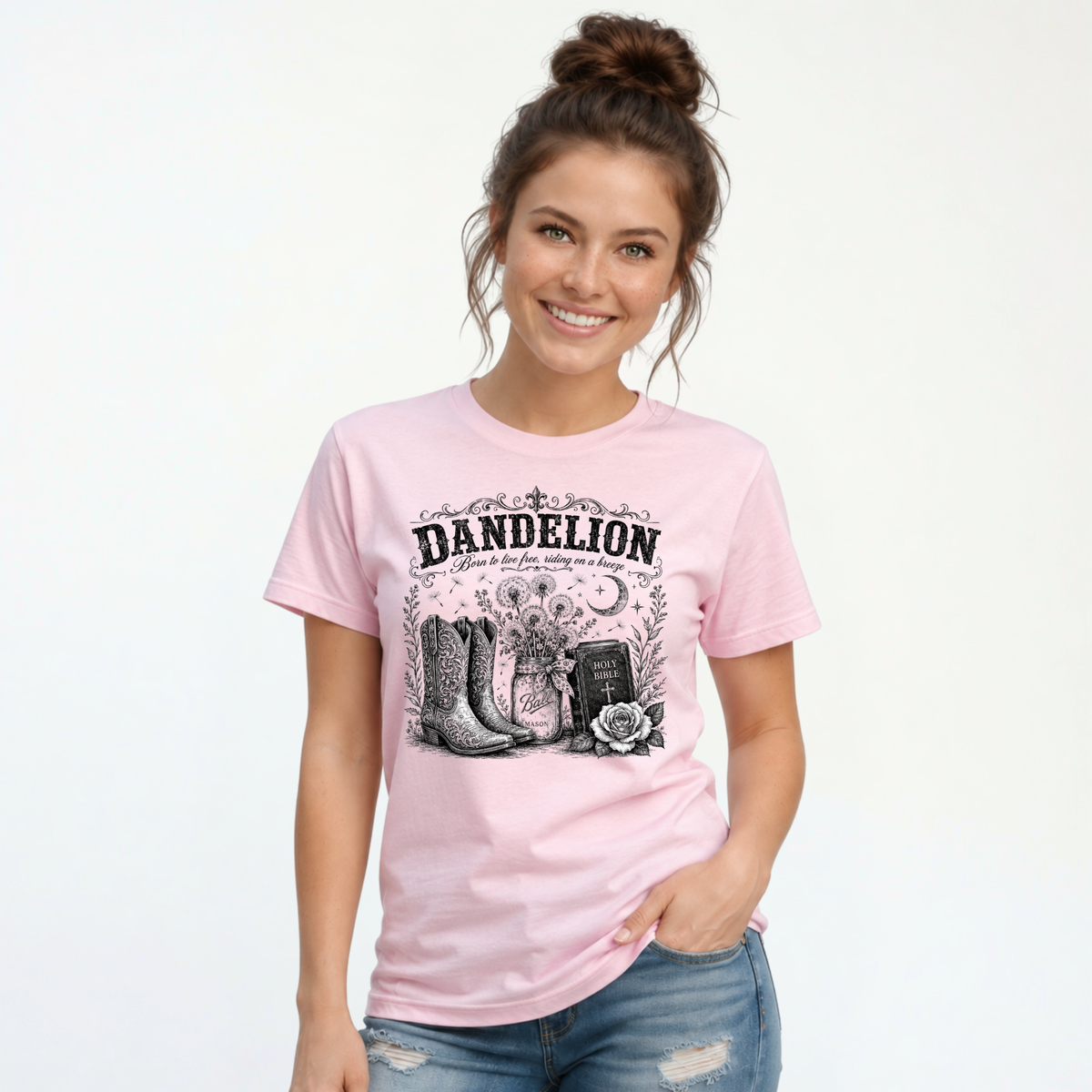Woman wearing a light pink Dandelion T-shirt with cowboy boots, dandelion-filled mason jar, Holy Bible, rose, and crescent moon graphic on a white background