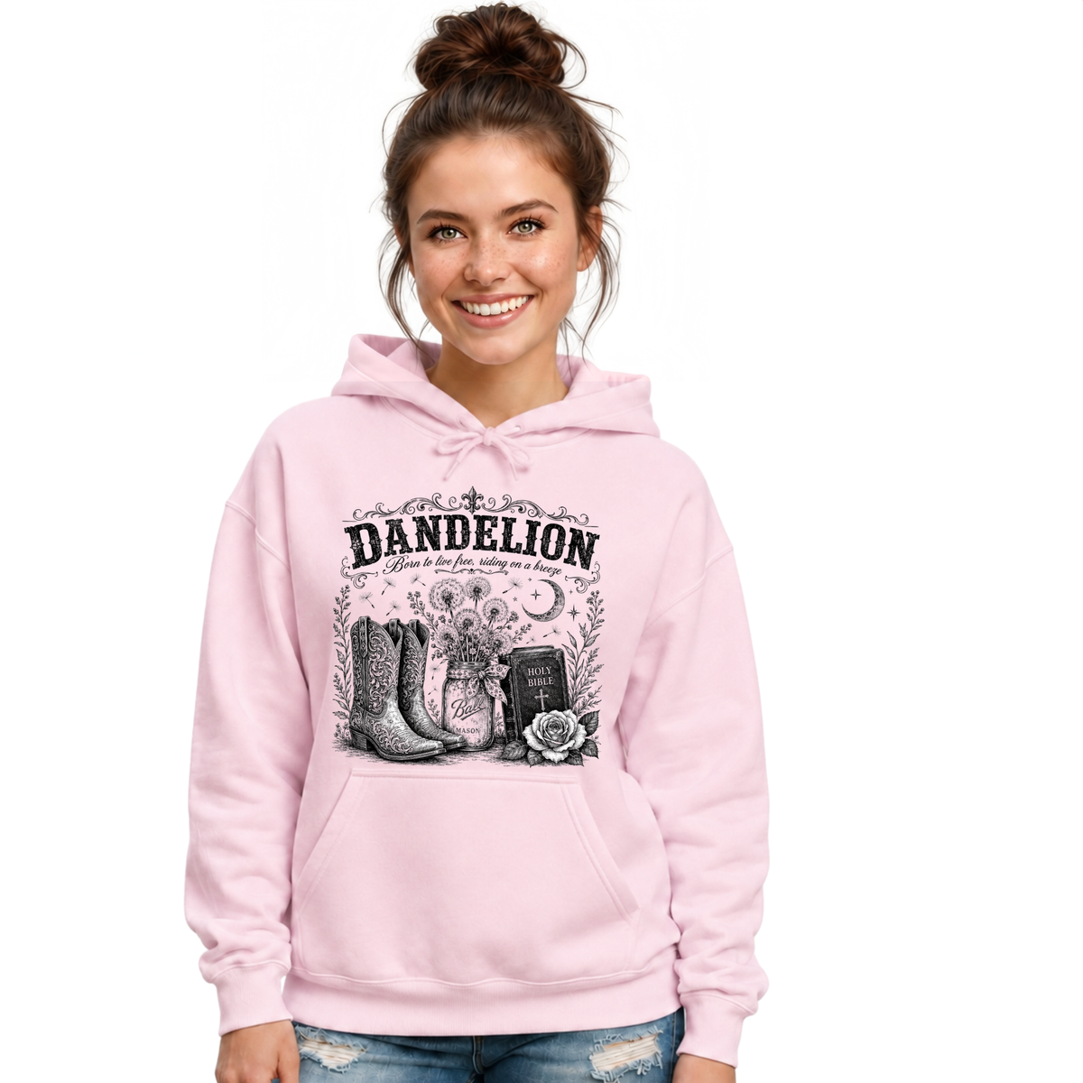 Woman wearing a light pink Dandelion pullover hoodie with cowboy boots, dandelion-filled mason jar, Holy Bible, rose, and crescent moon graphic on a white background
