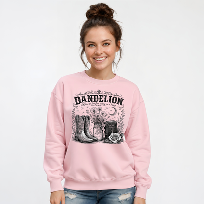 Woman wearing a light pink Dandelion crewneck sweatshirt with cowboy boots, dandelion-filled mason jar, Holy Bible, rose, and crescent moon graphic on a white background