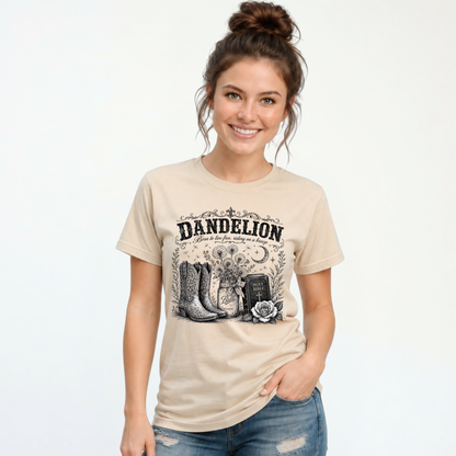 Woman wearing a sand Dandelion T-shirt with cowboy boots, dandelion-filled mason jar, Holy Bible, rose, and crescent moon graphic on a white background
