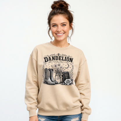 Woman wearing a sand Dandelion crewneck sweatshirt with cowboy boots, dandelion-filled mason jar, Holy Bible, rose, and crescent moon graphic on a white background