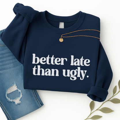 Dark navy blue sweatshirt with "Better Late Than Ugly" in bold white font. Folded neatly with denim and styled with gold necklace. Unisex fit perfect for women and teens. Cozy, humorous crewneck pullover for everyday wear or gifting.