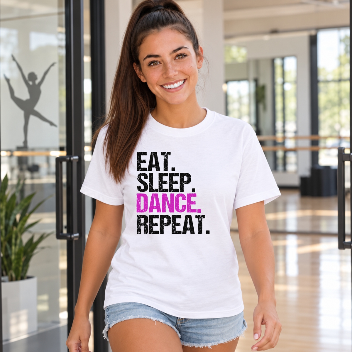Woman walking through a dance studio doorway in a white Eat Sleep Dance Repeat T-shirt.
