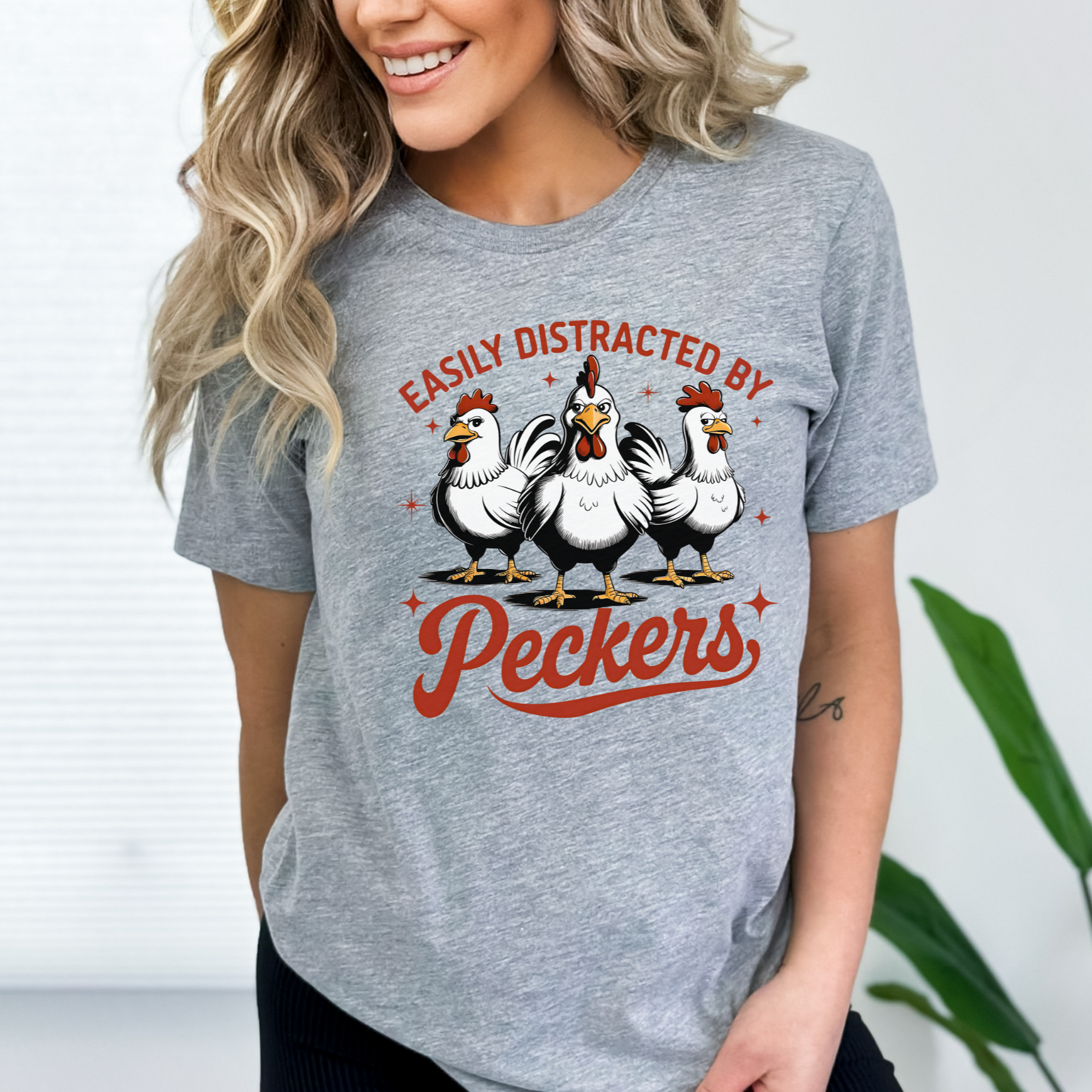  Woman wearing a Gray T-shirt with "Easily Distracted by Peckers" text and three funny chickens design. Perfect for chicken lovers and humor enthusiasts