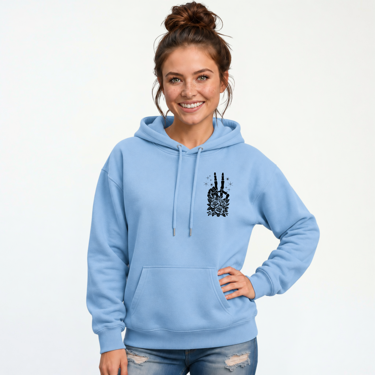 Woman wearing a light blue hoodie with a small black floral skeleton peace-sign graphic on the left chest.
