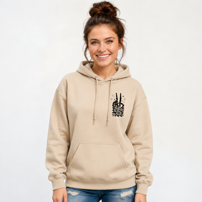 Woman wearing a sand hoodie with a small black floral skeleton peace-sign graphic on the left chest.