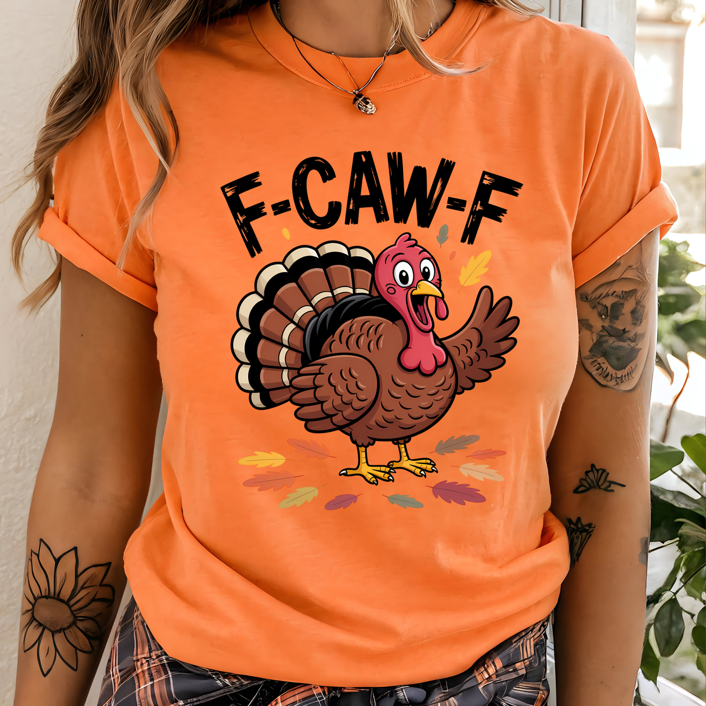 Woman wearing orange “F-CAW-F” turkey shirt, standing indoors with tattooed arm visible