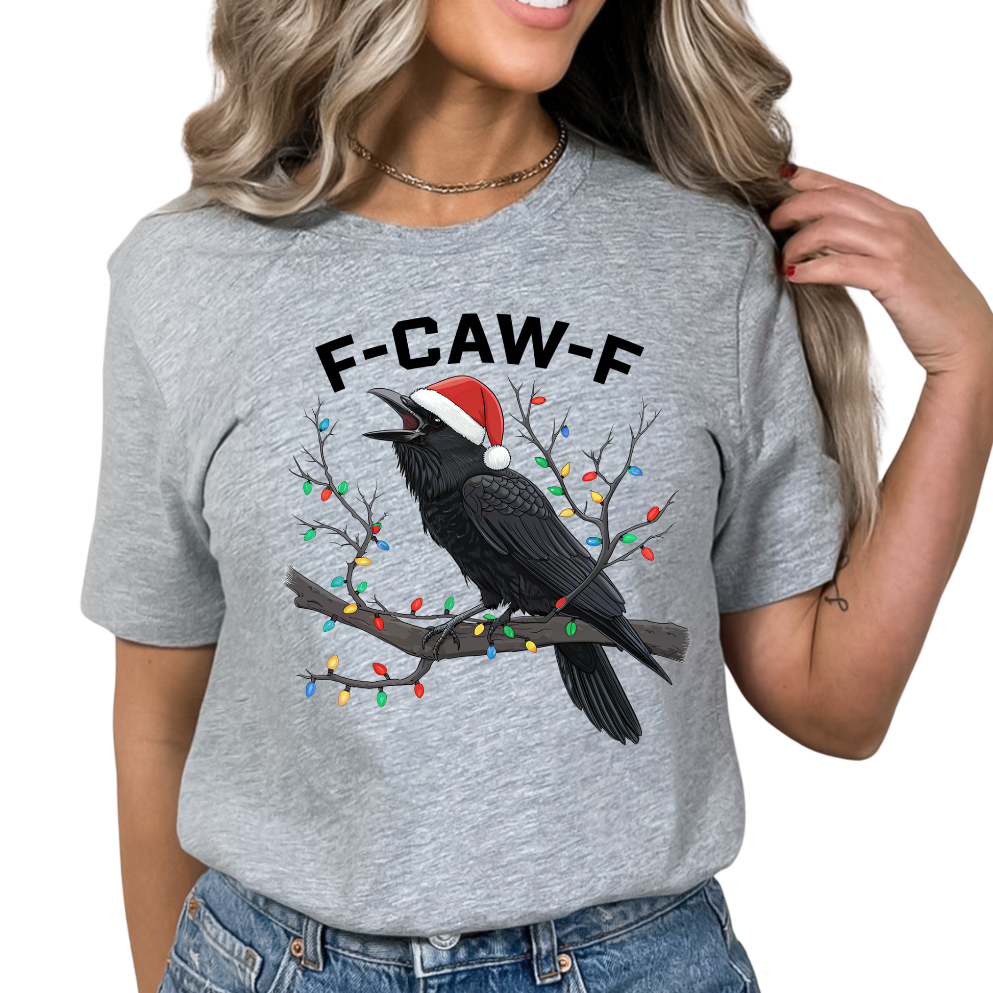 Woman in gray Christmas humor shirt featuring crow with Santa hat and lights.