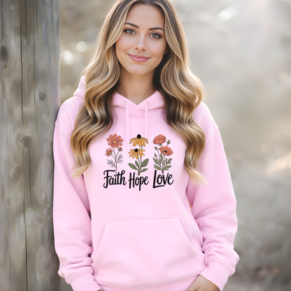 Woman wearing a pink hoodie with floral designs and 'Faith Hope Love' text against a wooden background.