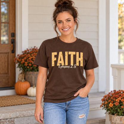 Woman modeling a brown T-shirt featuring distressed gold FAITH text and white Ephesians 2:8 script on a pumpkin-decorated autumn porch.